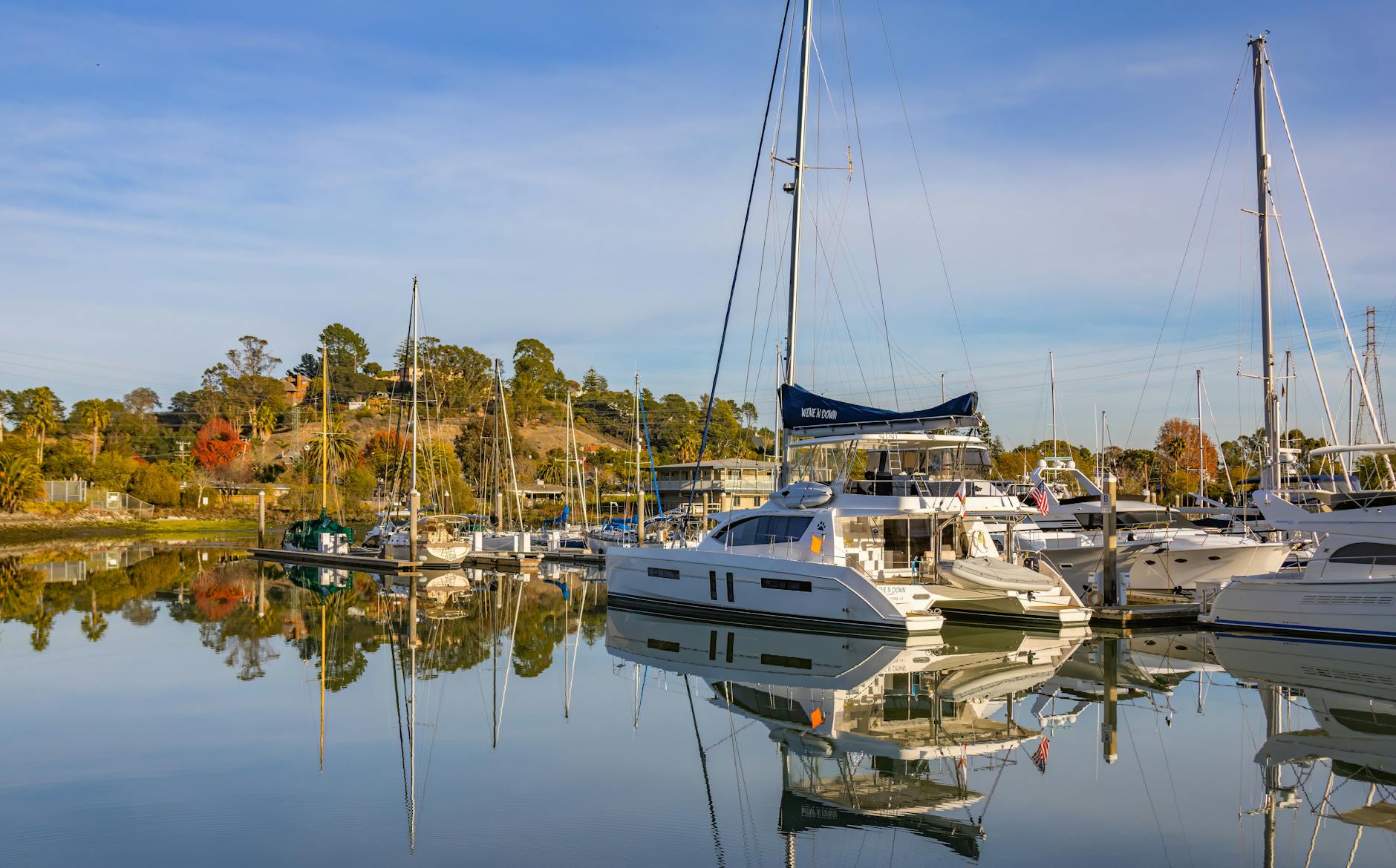 A peaceful marina scene with yachts reflecting in calm water, under a clear blue sky.