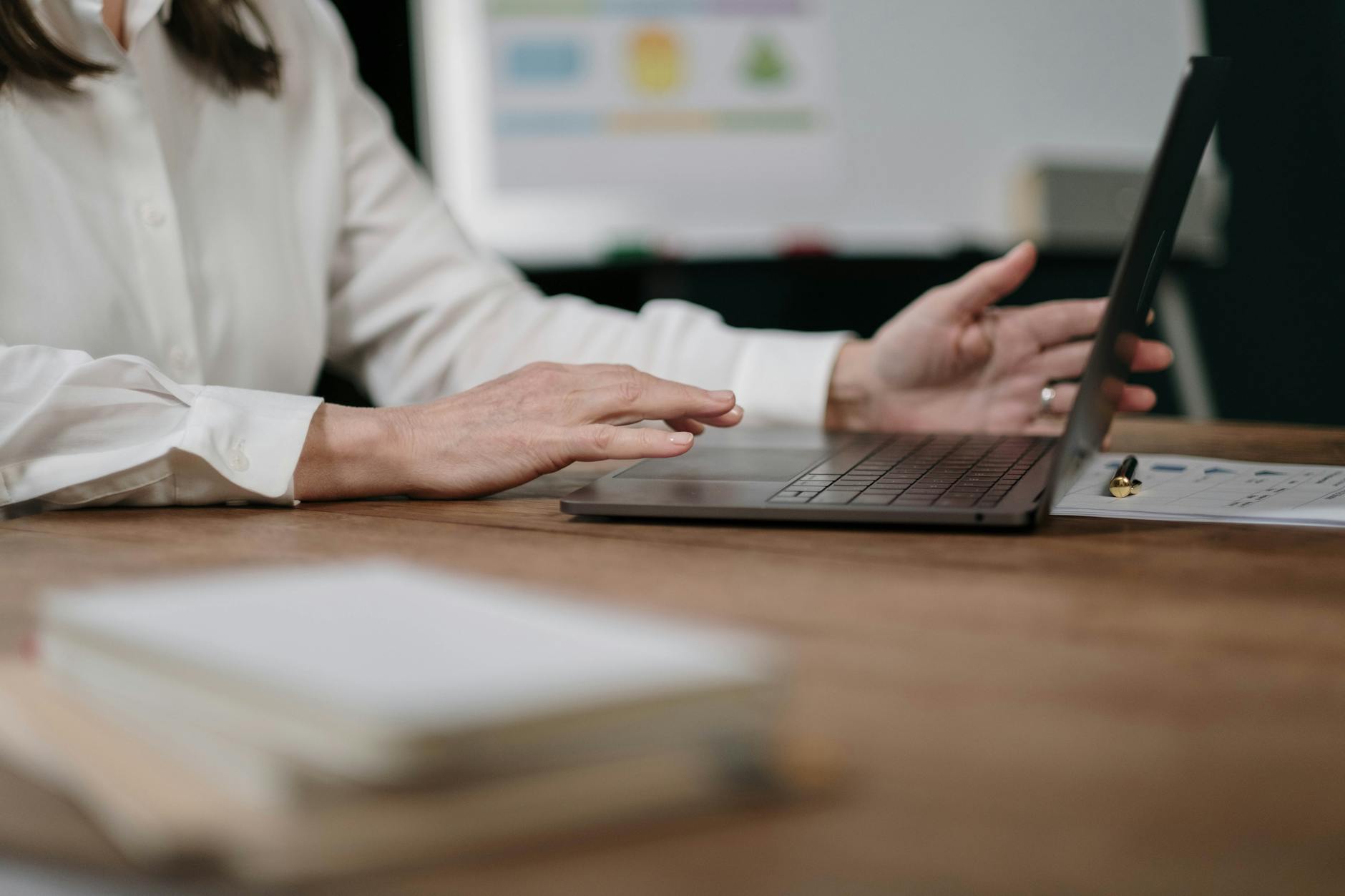 Close-up of an adult using a laptop on a wooden desk in an office setting.
