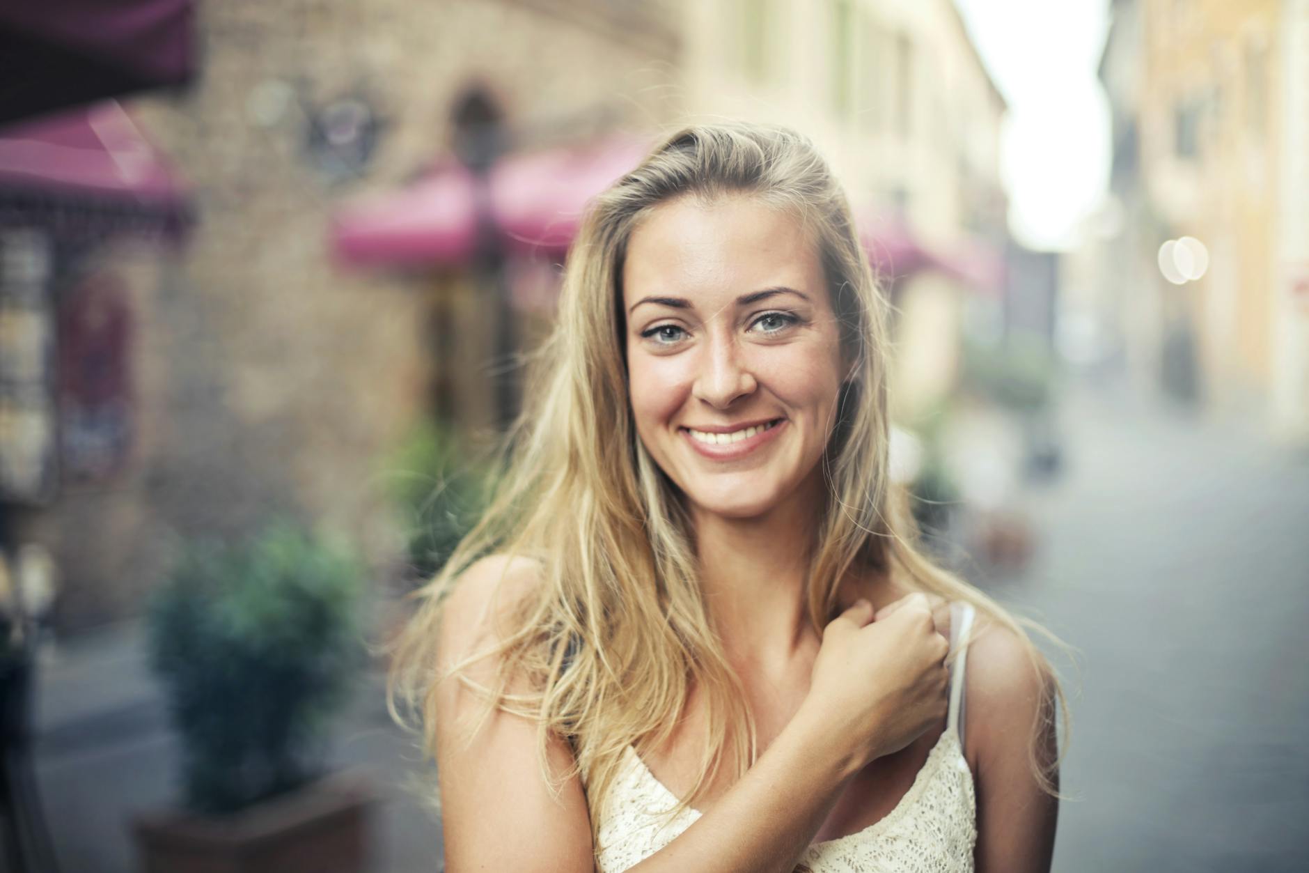 A happy woman with long hair poses on a sunny street, exuding joy and casual elegance.