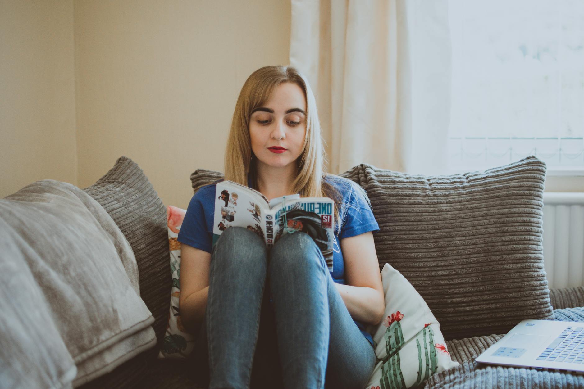 A woman enjoys reading manga while sitting comfortably on a cozy sofa, creating a relaxing atmosphere.