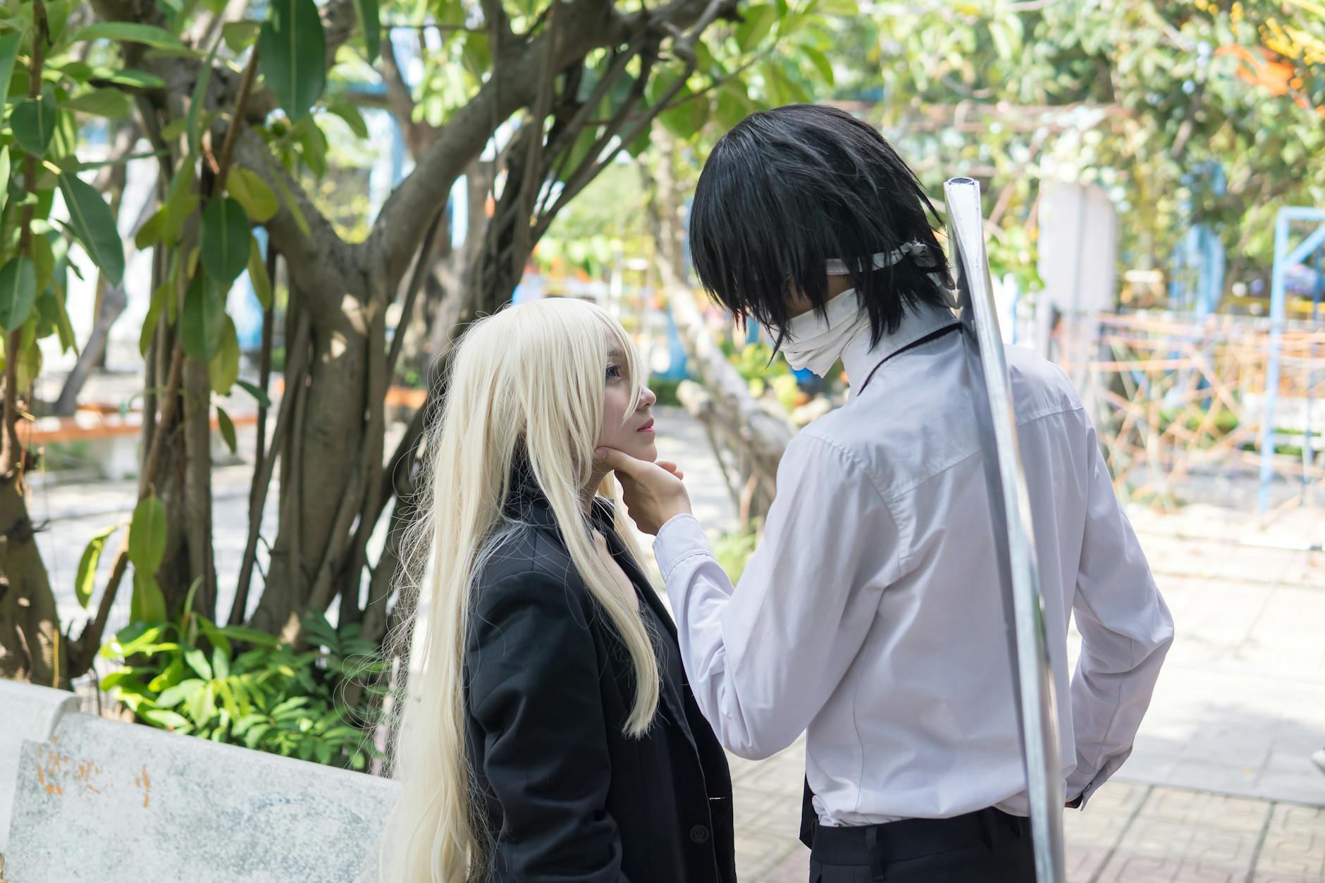 Two cosplayers in an engaging scene outdoors, surrounded by trees and greenery.
