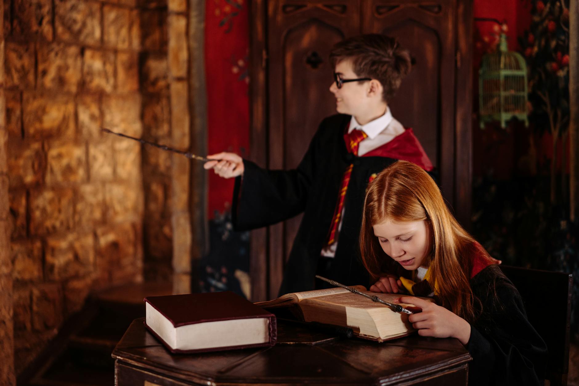 Two children dressed as wizards using magic wands and reading a spell book indoors.