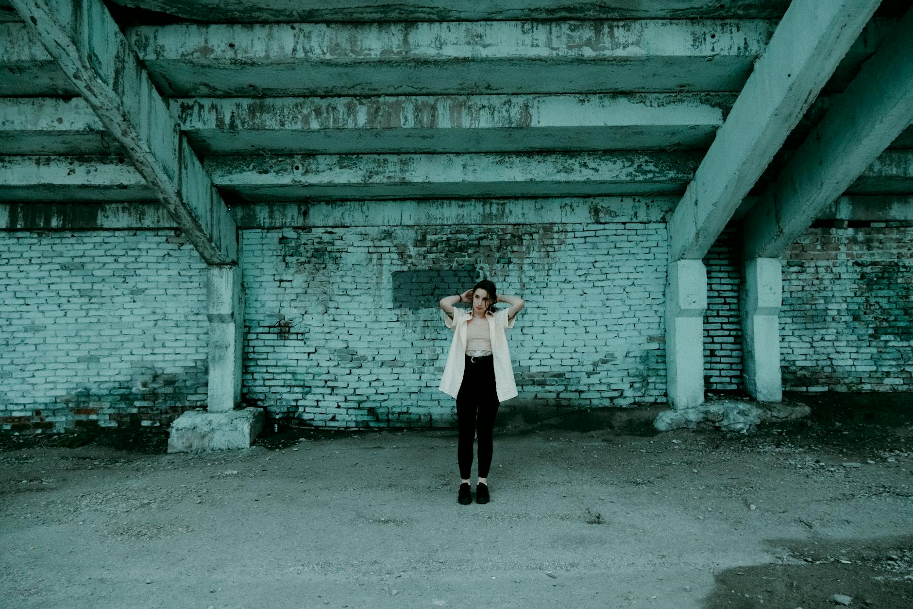 Woman posing under gritty urban structure with brick walls and concrete floor.