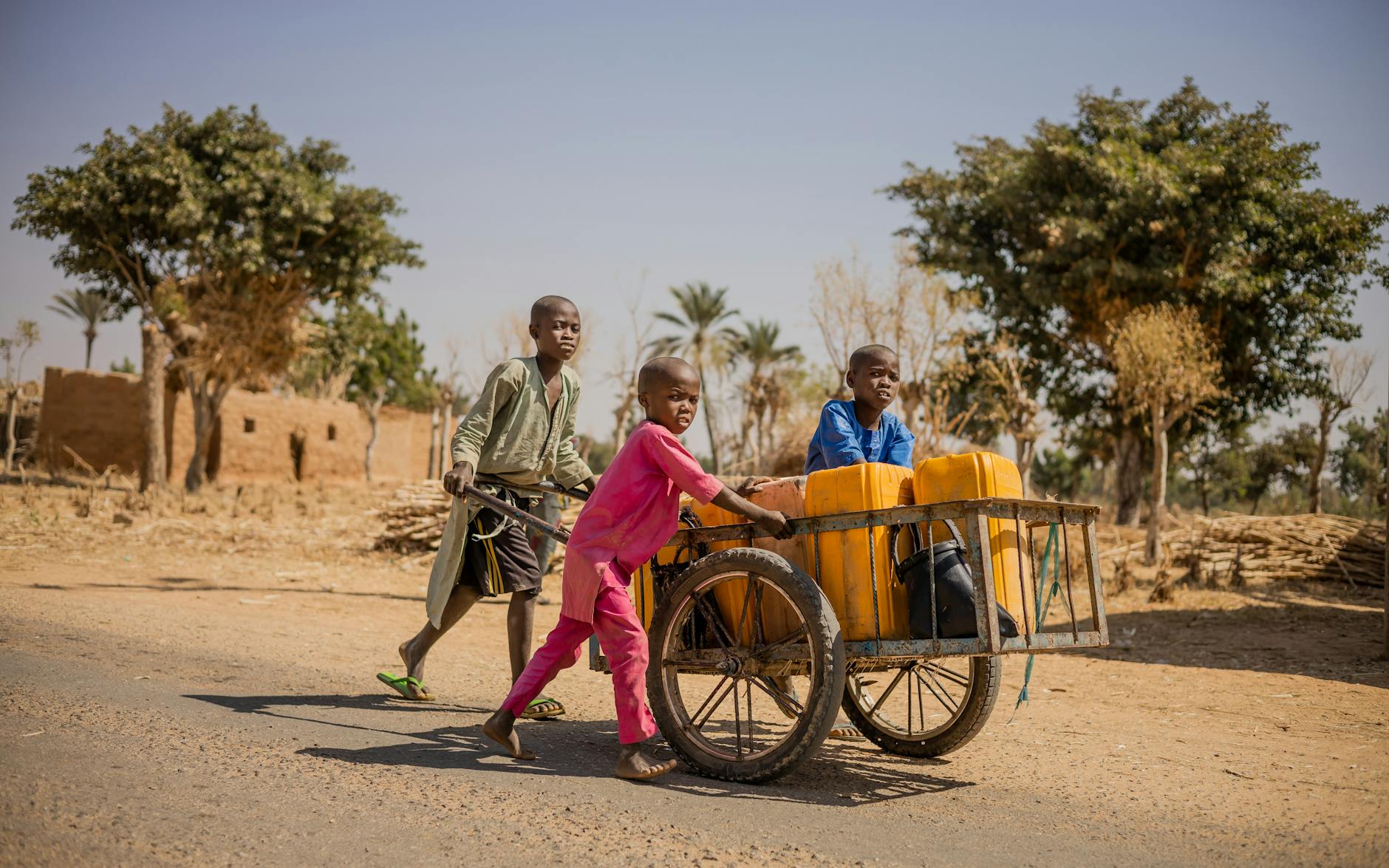 Three children in Nigeria pushing a cart with jerry cans, showcasing community resilience.