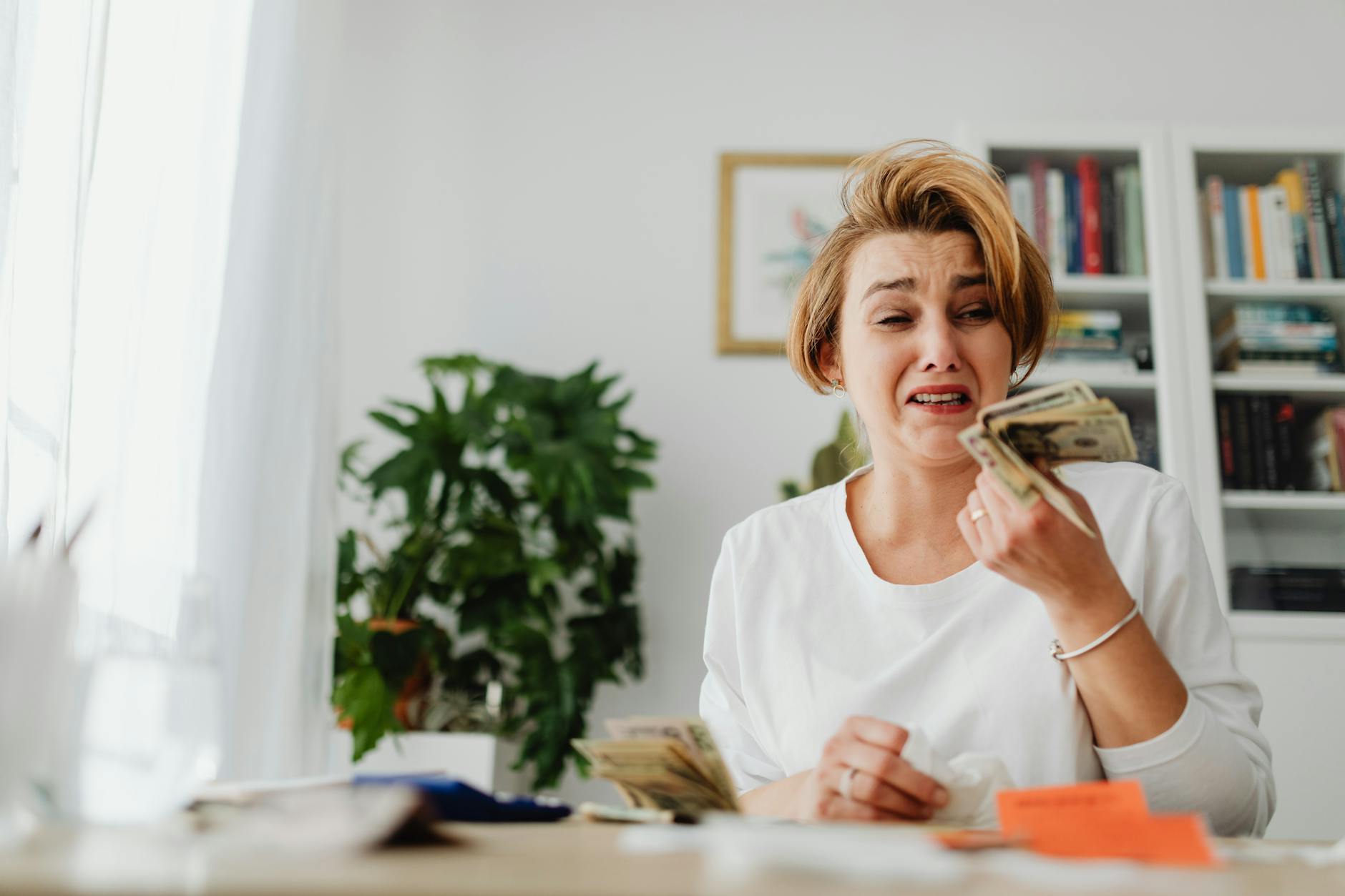 A woman looking stressed while counting money in a living room setting.