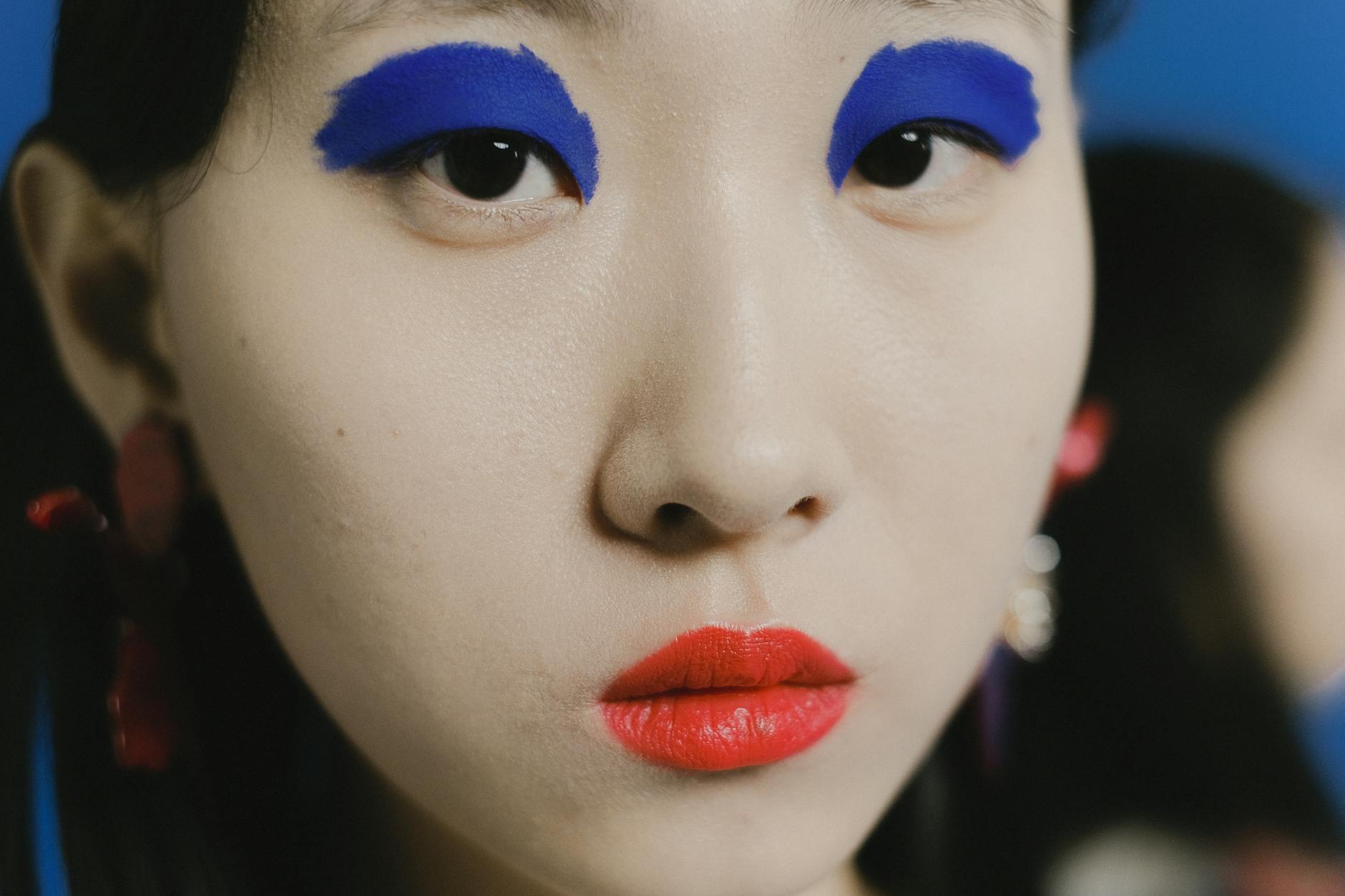 Striking close-up portrait of a person with bold blue eyeshadow and red lipstick.