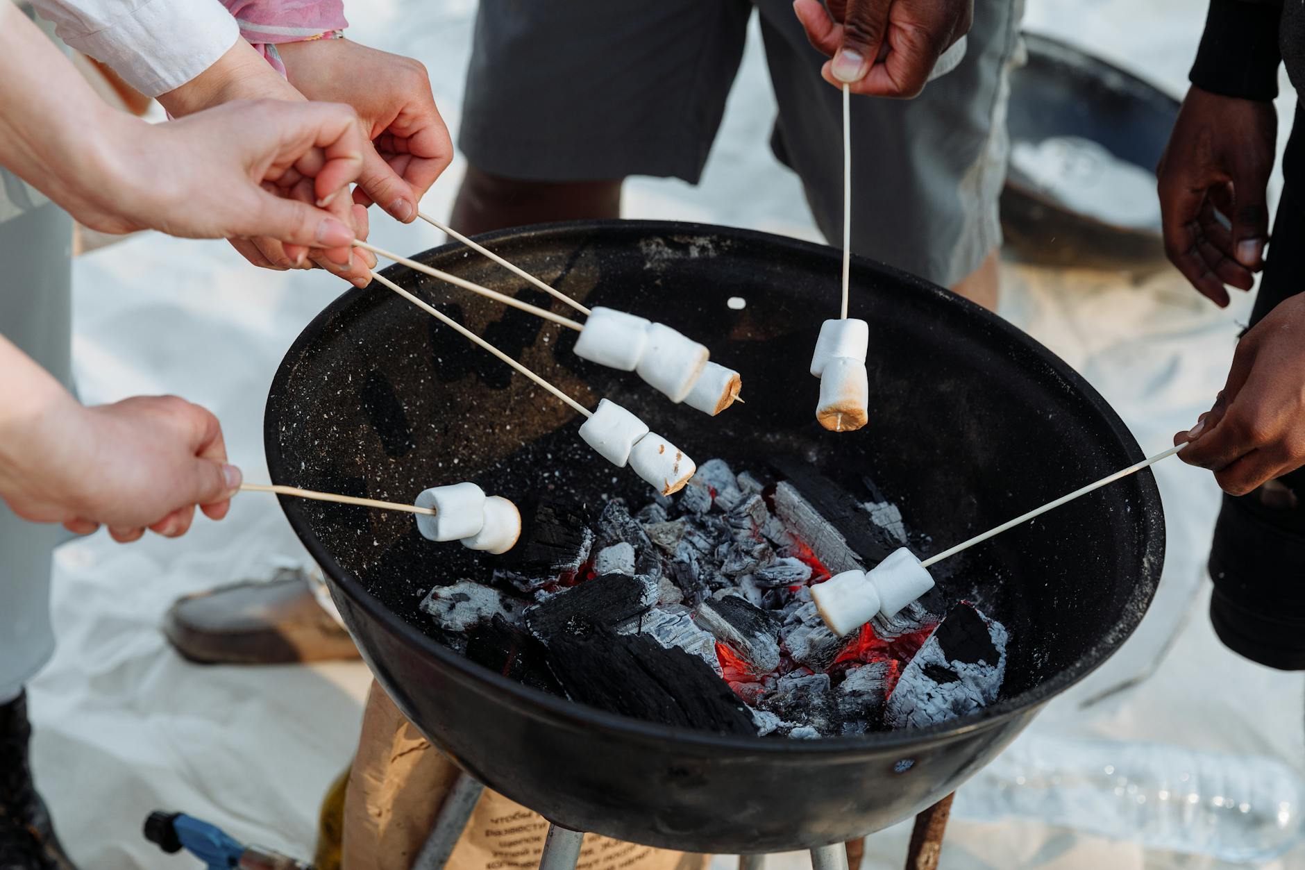 A group of people roasting marshmallows over a charcoal grill at the beach. Perfect summer activity.