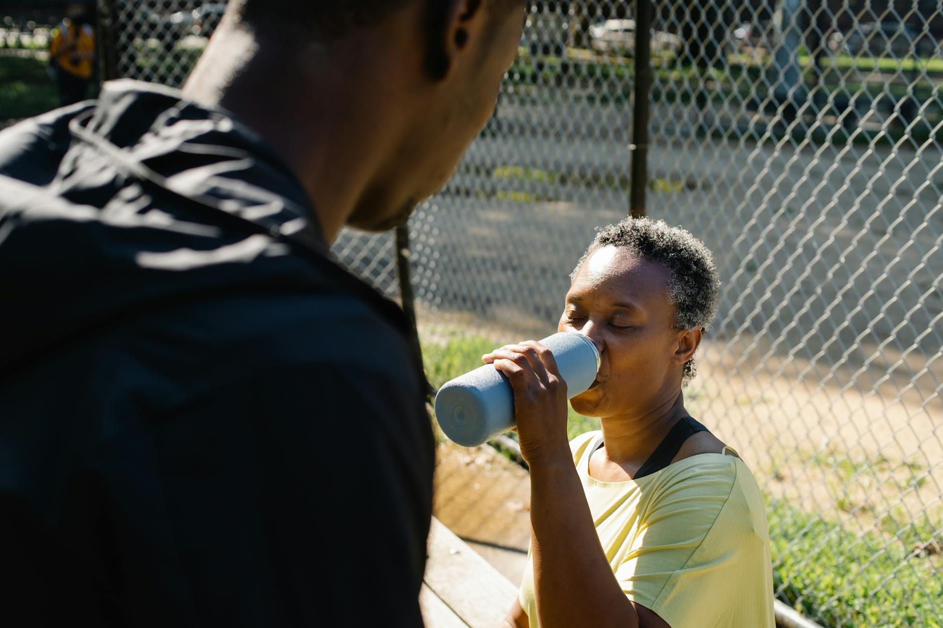 A woman and her child enjoying a break and hydrating outdoors in a sunny park.