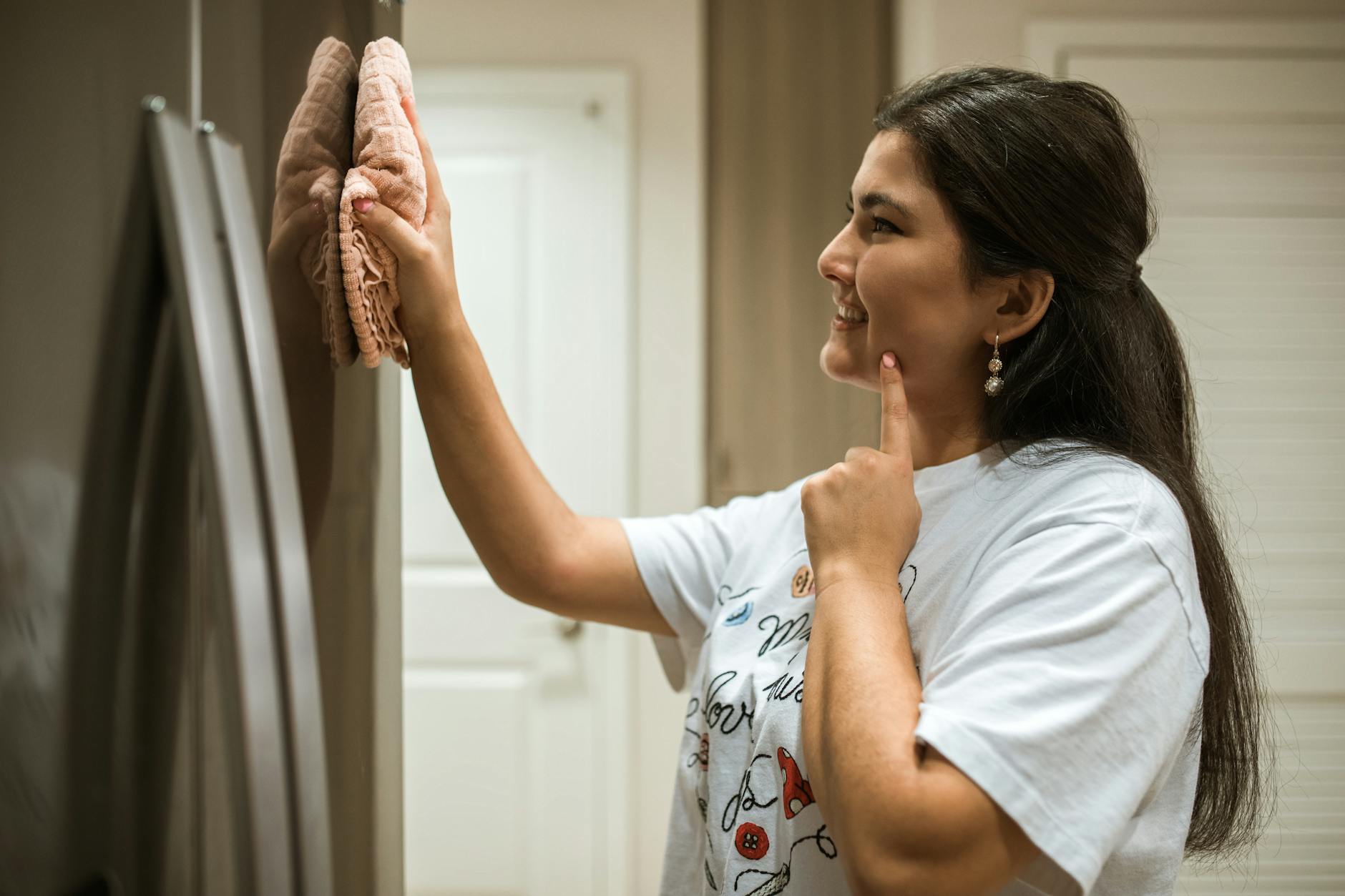 A woman cheerfully wipes a refrigerator, showcasing a moment of home cleaning.