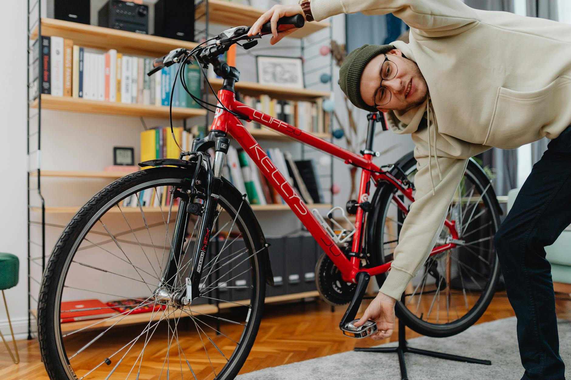 Young adult adjusting a bicycle pedal indoors, showcasing hands-on repair skills.