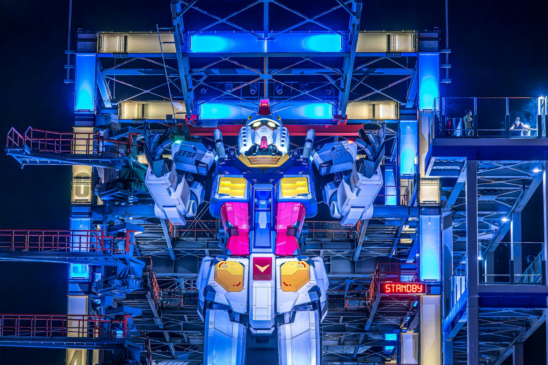 Illuminated Gundam robot at Yokohama's Gundam Factory lit up at night. Vibrant colors and futuristic design.