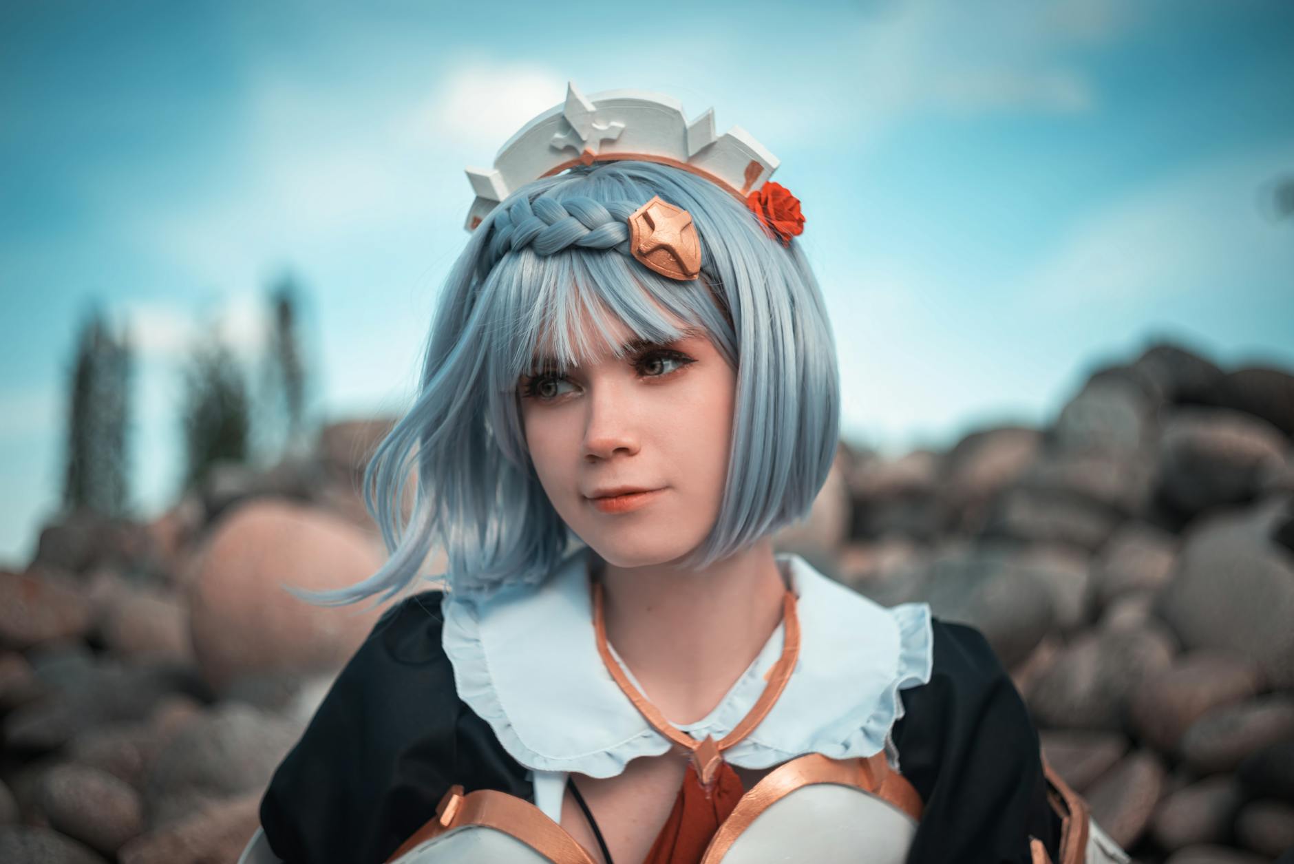 A cosplayer with blue hair and detailed costume posing in an outdoor setting with rocks.