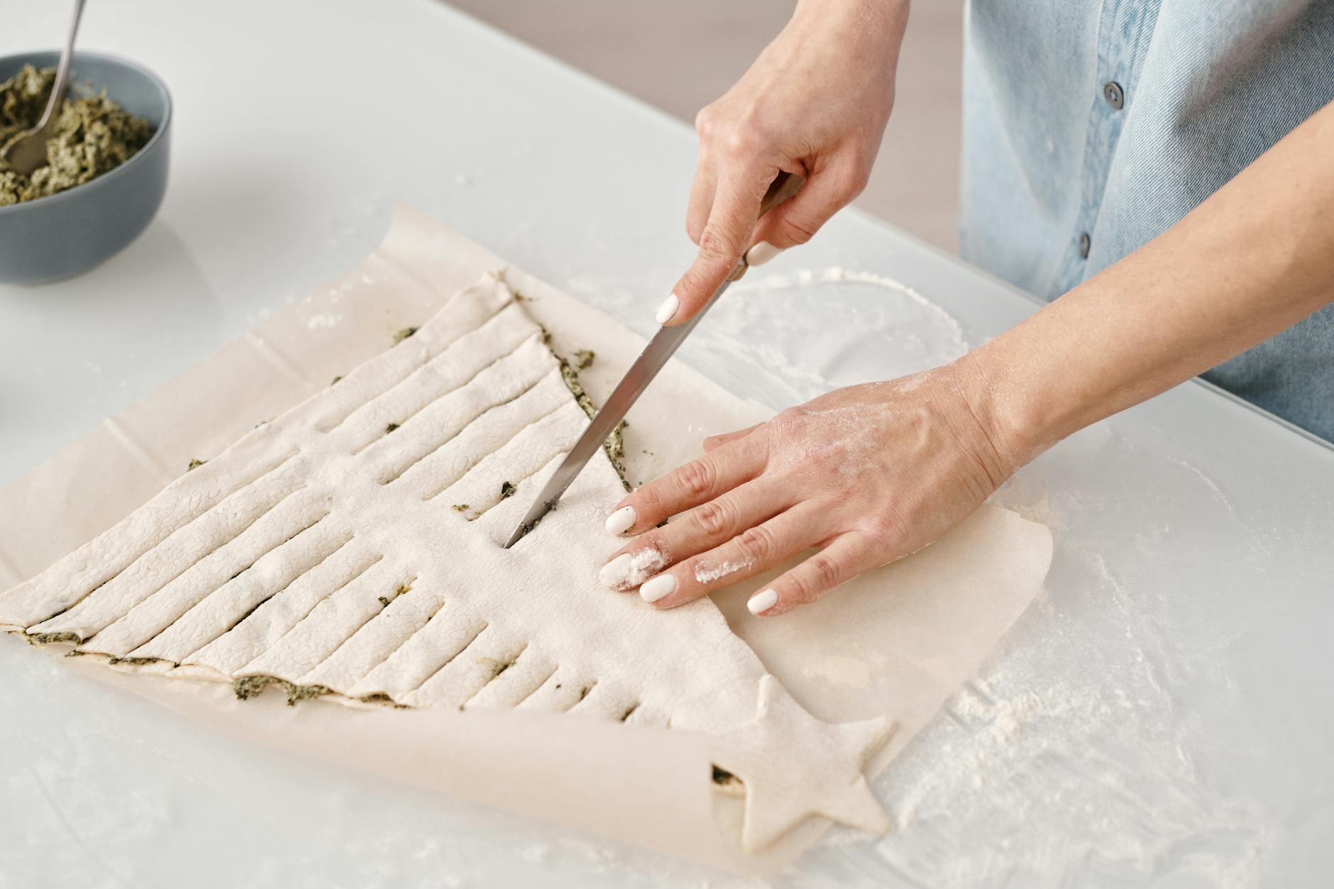 Close-up of hands slicing pastry dough in creative shape on kitchen counter.