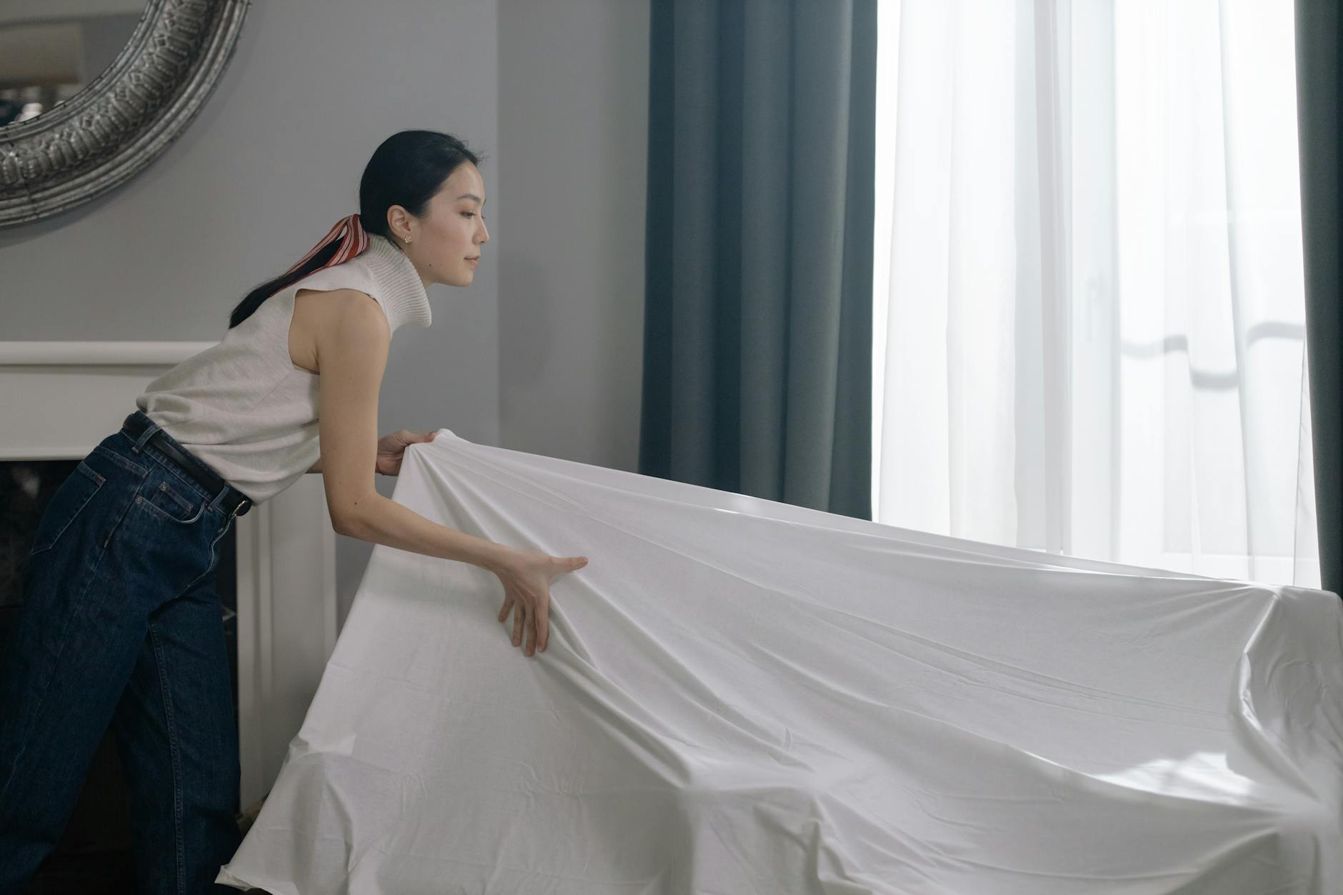 Woman adjusting white curtains indoors, enhancing room decor.