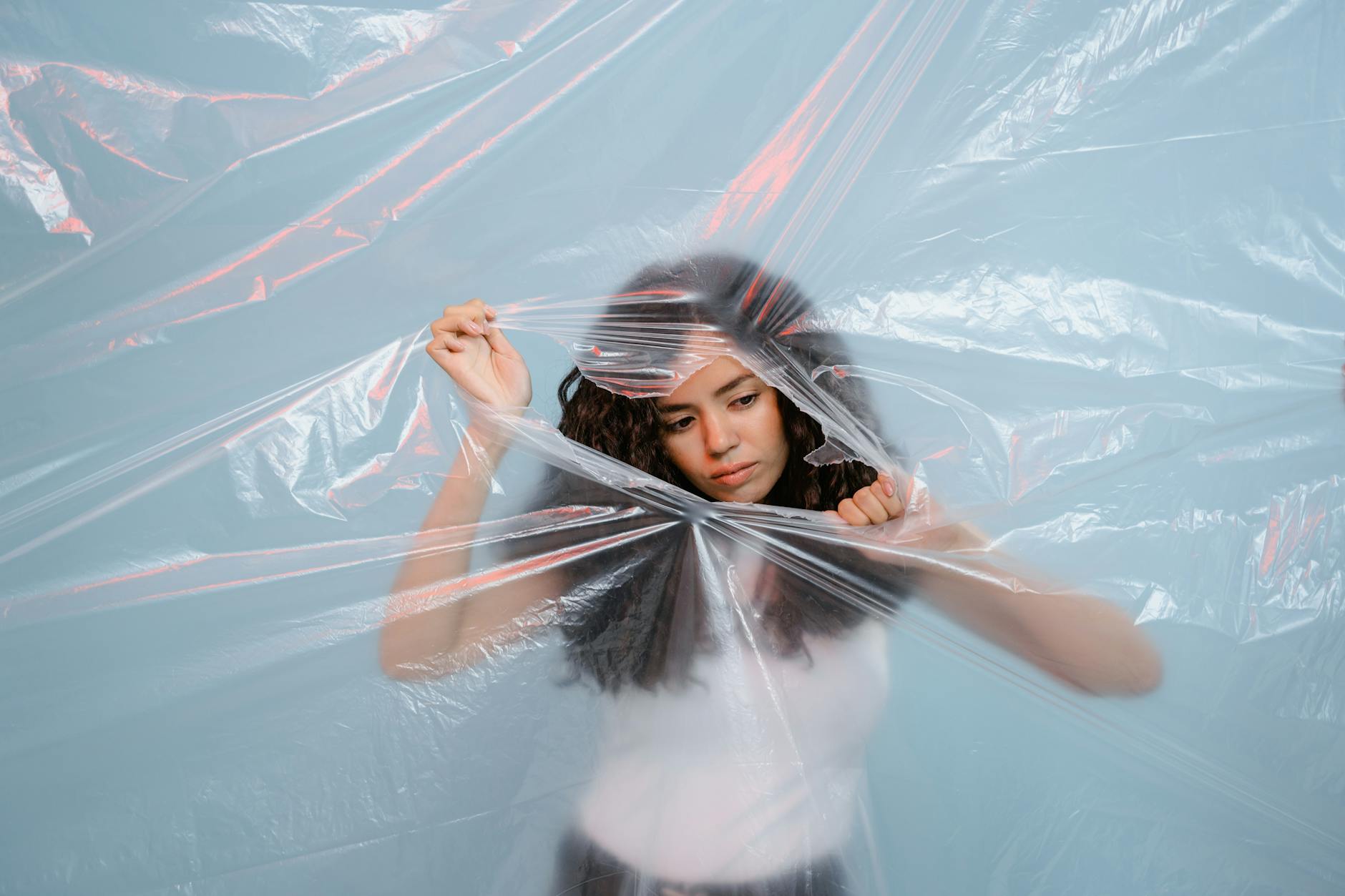 A young woman pushing against a plastic sheet, symbolizing environmental awareness and zero waste.