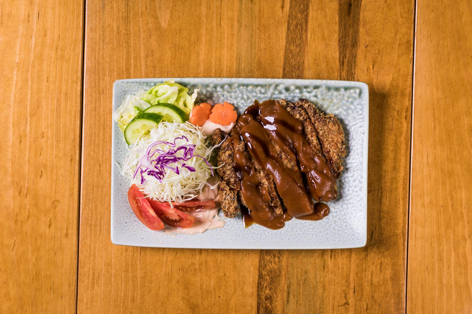 Crispy tonkatsu served with fresh vegetables on a ceramic plate, perfect for Asian cuisine lovers.