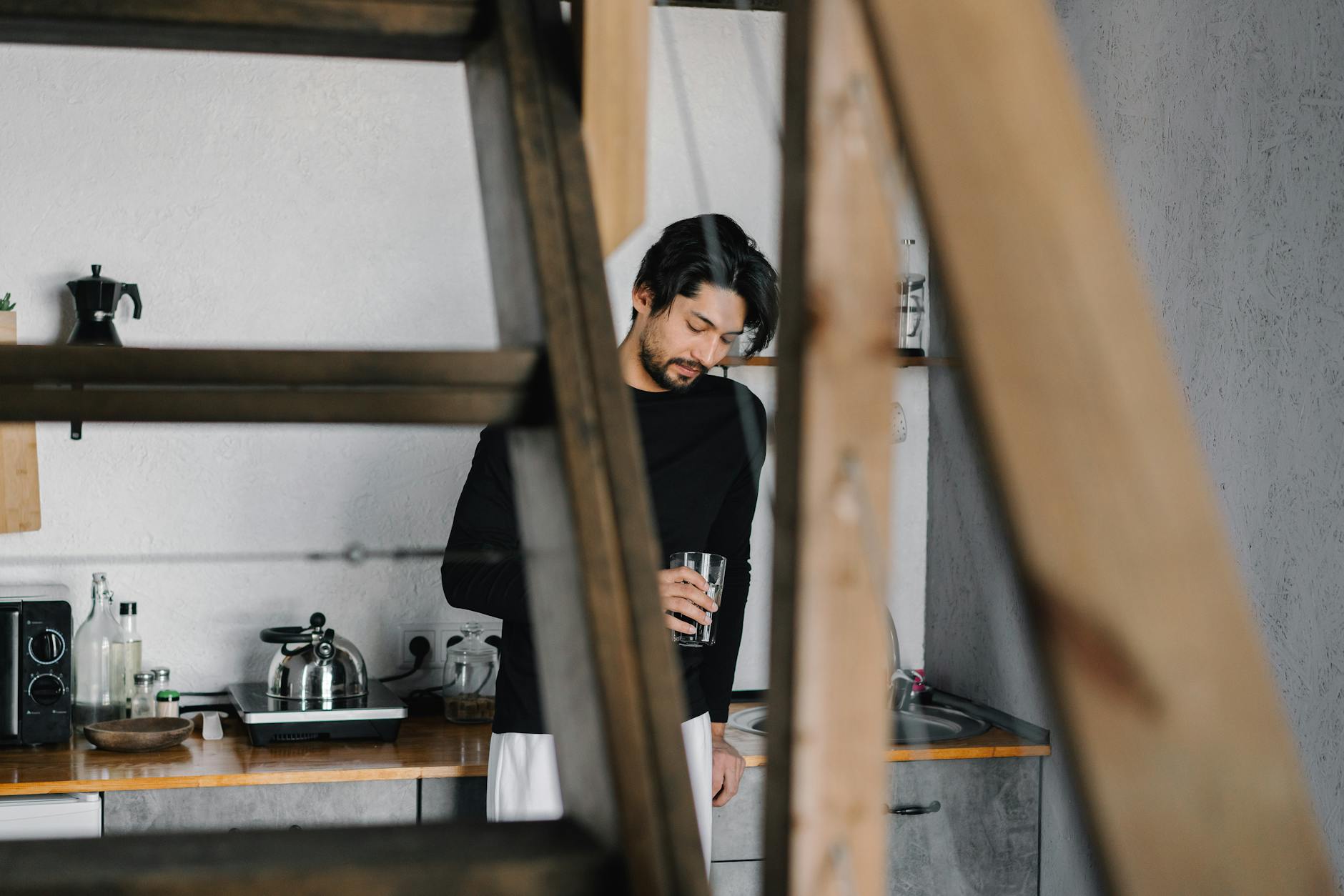 Capture of a man holding a drink in a stylish kitchen, exuding relaxation.