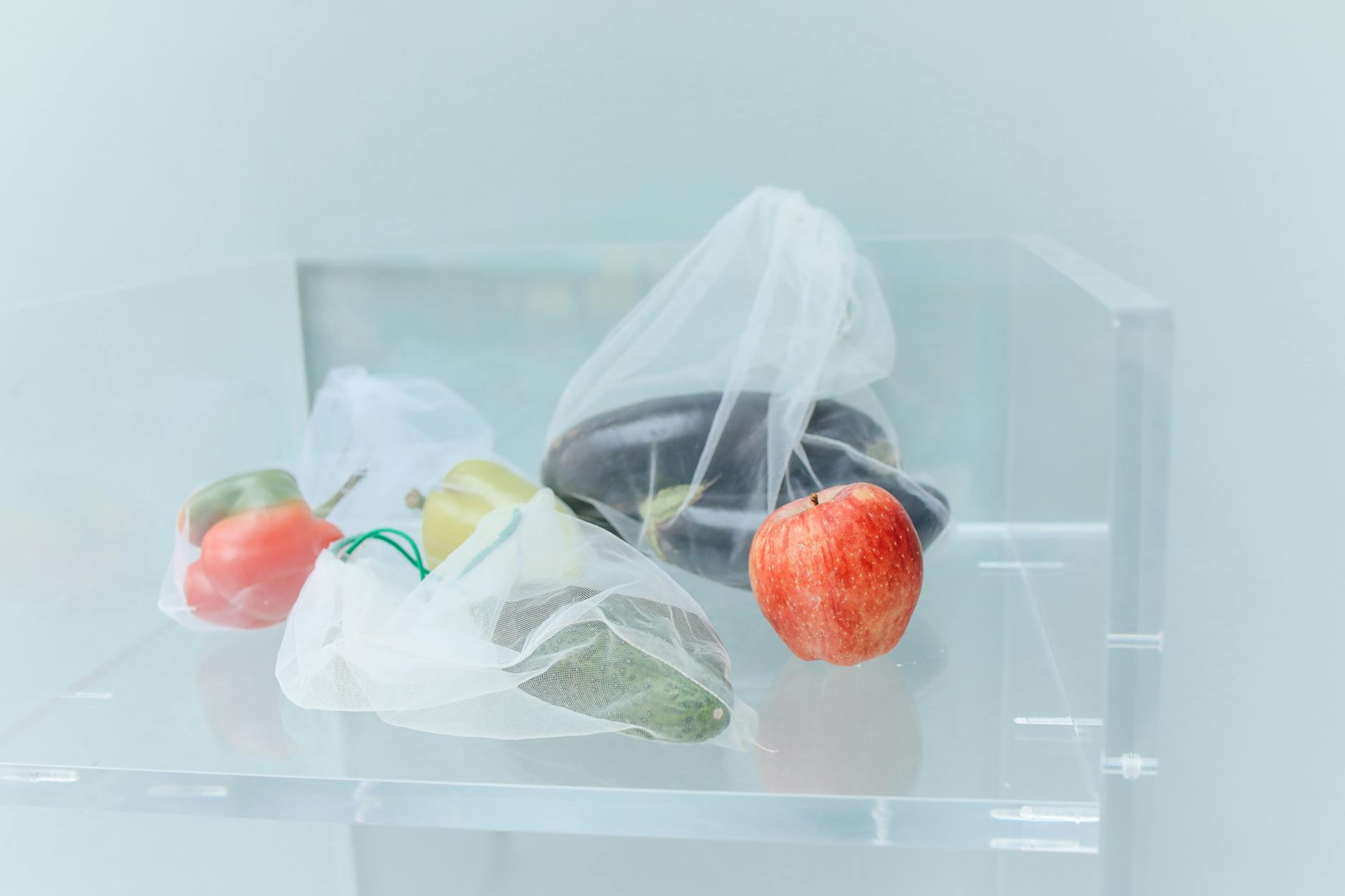 Reusable produce bags filled with fresh vegetables and a red apple, promoting eco-friendly shopping.